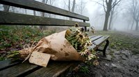 Wilted flower bouquet wrapped in kraft paper with a sorry tag on a wooden park bench in foggy autumn atmosphere.