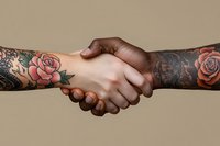 Close-up of tattooed arms with floral designs in handshake gesture against neutral background, symbolizing agreement, partnership and unity in business or personal relations.