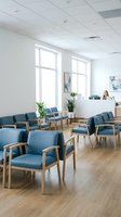 Modern medical office waiting room with blue chairs and wooden frames, bright natural light from large windows, professional healthcare interior design.