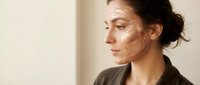 Young woman applying facial contouring makeup with highlighter and bronzer in natural lighting for beauty routine and cosmetic enhancement.