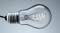 Clear glass light bulb with spiral filament and metal base against gray background, symbolizing innovation, creativity, and electrical technology.
