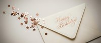 Elegant cream envelope with rose gold Happy Birthday script surrounded by scattered metallic star and circle confetti on a light background.