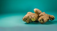 Fresh ginger root with cut piece showing green flesh interior on turquoise background, raw organic spice ingredient for cooking and natural medicine.