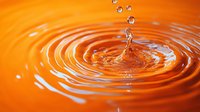 Clear water drop splash creating concentric ripple circles against vibrant orange background, captured in macro photography with floating droplets and dynamic liquid motion.