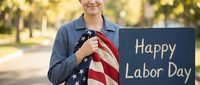 Young woman holding American flag with Happy Labor Day chalkboard sign outdoors in autumn park setting for patriotic holiday celebration.
