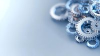 Metallic silver gears and cogs arranged on light blue background with selective focus and copy space, representing mechanical engineering and technology.