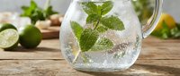 Refreshing sparkling water with fresh mint leaves and lime in glass pitcher on wooden table for summer beverages and healthy hydration concepts.