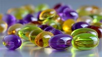 Colorful transparent gel capsules in purple, yellow and green colors on reflective surface with soft focus background creating medical concept.