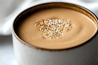 Creamy chocolate smoothie topped with sesame seeds in gray ceramic cup, close up view with soft focus and blurred background for food photography.