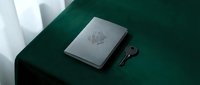 Closed gray notebook with embossed seal and vintage key on dark green fabric surface, minimalist flat lay composition for branding and editorial design projects.