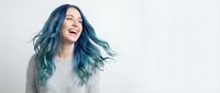 Young woman with vibrant blue green ombre hair laughing joyfully against white background. Carefree expression shows happiness and positive energy.