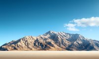 Majestic mountain peak rising above desert landscape with dramatic rock formations against vibrant blue sky with scattered white clouds, creating serene wilderness scenery.
