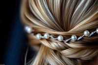 Elegant blonde hair updo decorated with pearl and crystal hairpiece, close-up view showing intricate twisted strands and bridal hair accessories against dark background.