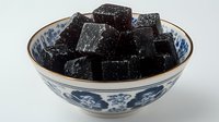 Black grass jelly dessert cubes in traditional Asian blue and white porcelain bowl with floral pattern. Popular cooling sweet treat in Chinese cuisine.