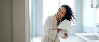 Young African American woman in white bathrobe laughing joyfully in modern bathroom after shower, expressing happiness and self-care wellness lifestyle.