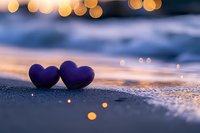 Two purple hearts on sandy beach at sunset with golden bokeh lights creating romantic atmosphere for love and relationship concepts.