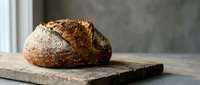 Freshly baked artisan sourdough bread loaf with golden crust on rustic wooden cutting board in modern kitchen setting for bakery and food photography.