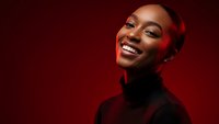 Happy young African American woman laughing with joy wearing black turtleneck against red background. Studio portrait for lifestyle and wellness content.