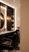 Modern luxury salon interior with black styling chairs, illuminated mirror, and organized product shelves for professional hair and beauty services.