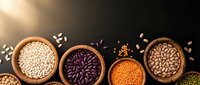 Assorted legumes and grains in wooden bowls on dark background with scattered seeds, healthy protein sources for cooking and nutrition.