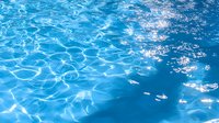 Bright sunlight reflects on rippling blue swimming pool water creating mesmerizing caustic patterns and light reflections. Serene summer aquatic background.