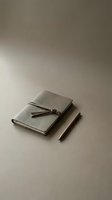 Minimalist leather journal notebook with tie closure and wooden pen on neutral beige background for writing planning and creative work.