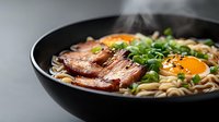 Asian noodle soup with sliced pork belly, raw egg yolk, green onions and sesame seeds in black ceramic bowl on gray background. Traditional ramen.