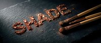 Crushed cocoa powder arranged on dark slate surface with makeup brushes, suitable for cosmetics, beauty, and culinary content.