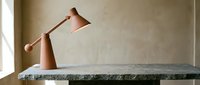 Adjustable copper desk lamp with wooden base on stone table in minimalist interior space.