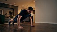 Fit male athlete performing push-up exercise on wooden floor in modern home gym, demonstrating strength training and fitness routine for workout and athletic conditioning.
