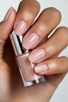 Elegant nude pink manicure on medium skin tone female hand holding nail polish bottle, showcasing glossy gel finish and perfectly shaped long nails.