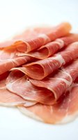 Thinly sliced prosciutto ham arranged on white surface, delicate cured meat with marbled texture for gourmet cooking and charcuterie board presentations.