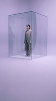 Young Asian woman in flowing gray dress standing inside transparent glass cube on purple gradient background for conceptual art and design projects.