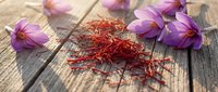 Red saffron threads with purple crocus flowers on rustic wooden background. Premium spice for culinary cooking and natural medicine ingredients.