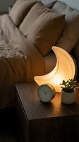 Cozy living room interior with glowing crescent moon lamp on wooden table beside clock and succulent plant creating warm ambient lighting atmosphere.