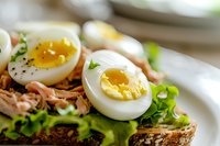 Open-faced sandwich with soft boiled eggs, flaked tuna, fresh lettuce on multigrain bread, extreme close up showing runny yolk and texture details in natural light.