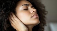 Young African American woman with natural curly hair in peaceful meditation pose with eyes closed and serene expression against blurred background.