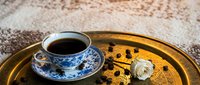 Black coffee in a blue and white porcelain cup on a golden tray with roasted beans and a white rose, elegant vintage style.