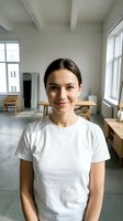 Young Caucasian woman in white t-shirt smiling at camera in bright modern office space with wooden furniture and large windows for business portrait.