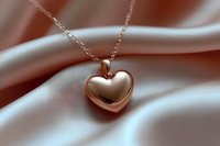 Rose gold heart pendant necklace on soft silky fabric background with gentle folds creating romantic mood and luxury jewelry presentation setting.