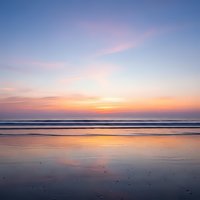 Tranquil ocean sunset with pastel sky colors reflecting on wet sand beach. Peaceful seascape with gentle waves and serene twilight atmosphere for relaxation.
