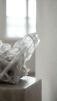 Clear crystal quartz mineral specimen on white pedestal in bright natural window light creating elegant shadows and reflections in minimalist interior space.