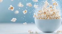 Fresh popcorn exploding from light blue ceramic bowl against soft blue background with floating kernels and magical sparkle effect creates festive mood.