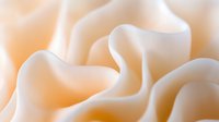 Soft flowing fabric in cream and peach tones creates gentle waves and folds with smooth curves and delicate shadows, suitable for luxury fashion and wedding backgrounds.