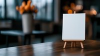 Small blank white canvas on wooden easel stand in cozy restaurant interior with warm lighting and blurred background for menu display or artwork presentation.