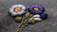 Delicate embroidered flowers with silver, purple and gold threads on natural linen fabric, showing intricate needlework details and textile artistry in macro view.