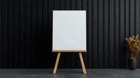 Blank white canvas on wooden easel against dark wall with dried flowers for art studio mockup and creative workspace design.