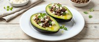 Halved avocados filled with seasoned ground meat and topped with fresh herbs, served on white plate for healthy lunch or dinner meal preparation.