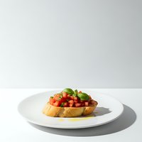Fresh bruschetta with diced tomatoes and basil on toasted bread served on white plate against clean background for culinary presentations and menu design.