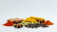 Colorful aromatic spices and herbs arranged on white background including turmeric, paprika, star anise, cardamom and black peppercorns for cooking.